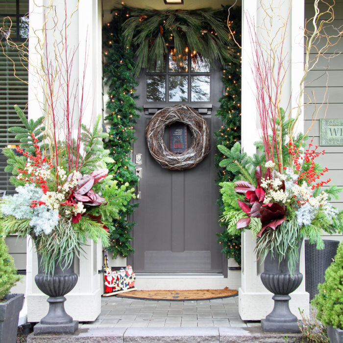 Beautiful home entrance decorated for Christmas. Festive front door with a holiday wreath, sparkling lights and and seasonal floral arrangements.